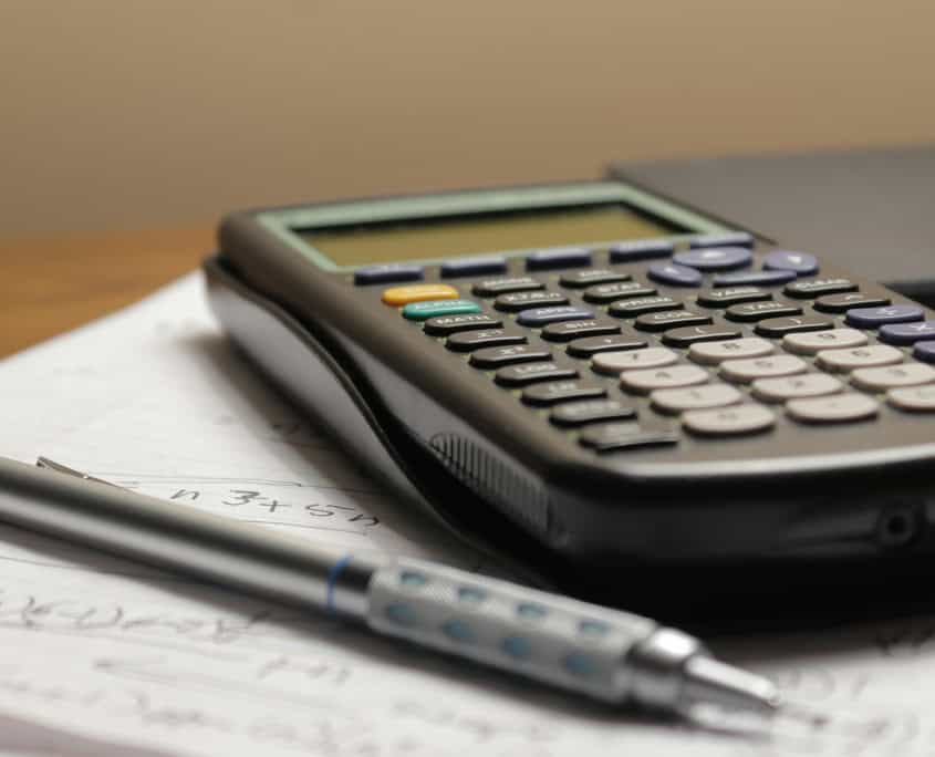 A calculator and pen rest on handwritten maths notes on a desk.