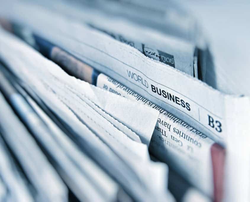 A close-up of stacked newspapers, with a visible headline reading “World Business” at the top.