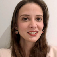 Woman with long brown hair, wearing red lipstick and pink earrings, smiling at the camera in front of a white wall.