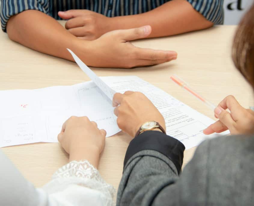Three people sit at a table, reviewing documents and discussing paperwork together.